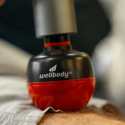 Red and black massage ball with 'wellbody' branding on a blurred background